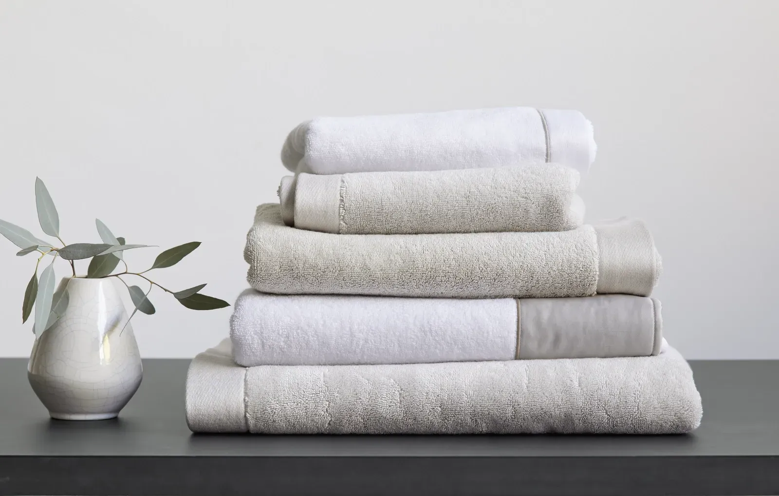 Ein Stapel weißer Handtücher liegt übereinander auf einem Tisch neben einer Vase.