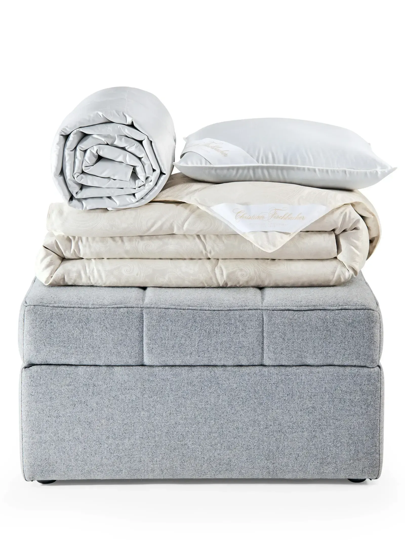 Ein Stapel Decken und Kissen auf einem grauen Ottomanen.