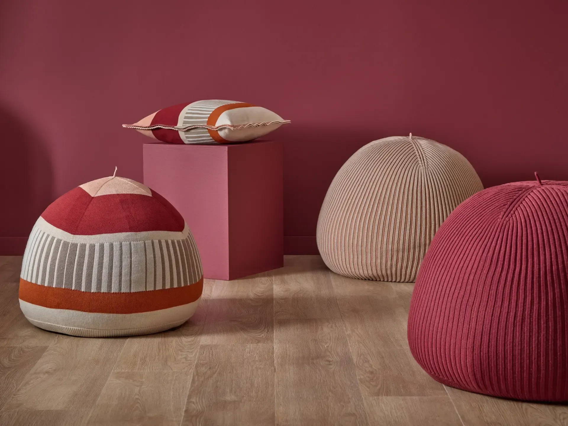 Eine Gruppe von Ottomanen und Kissen steht auf einem Holzboden vor einer roten Wand.