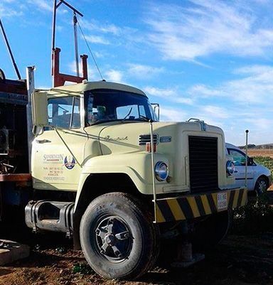 Un camión blanco con una franja amarilla al costado está estacionado en un campo de tierra.