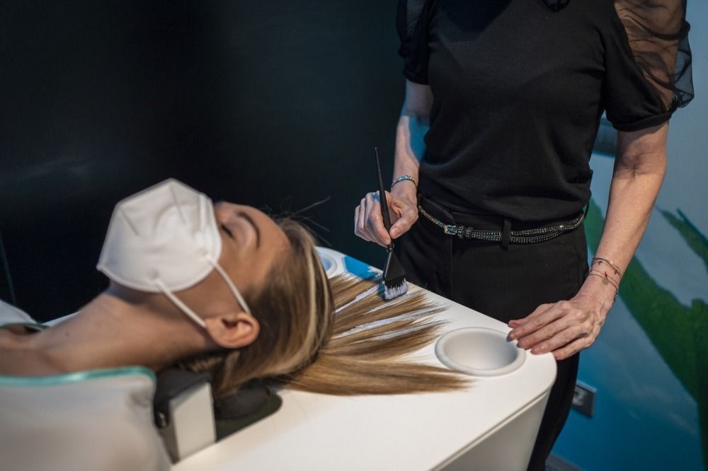 Una mujer que lleva una máscara se está tiñendo el pelo en un salón.