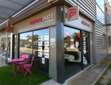 La façade d'une agence immobilière Stéphane Plaza, avec une table et des chaises roses installées à l'extérieur sur du gazon artificiel.