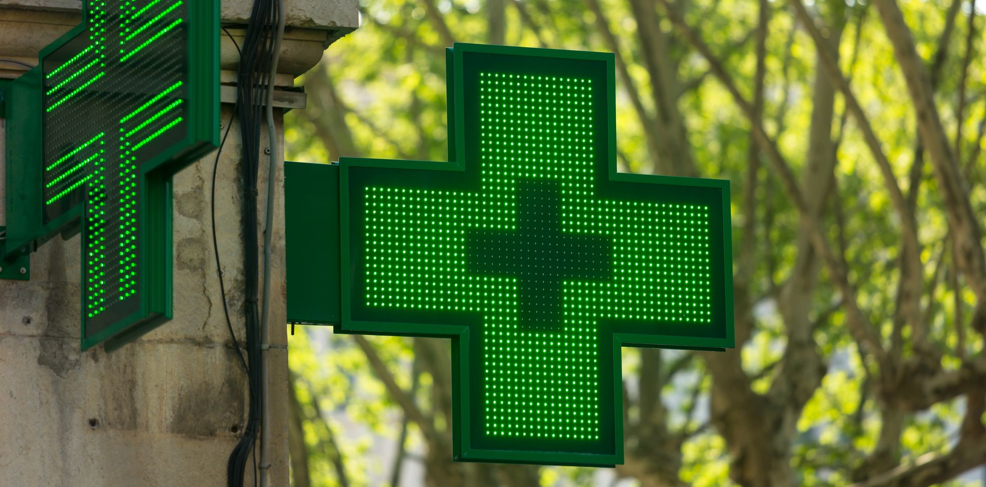 Extérieur d'un bâtiment de pharmacie moderne présentant une façade bleu foncé avec des accents verts et des enseignes indiquant PHARMACIE MÉDICALE.