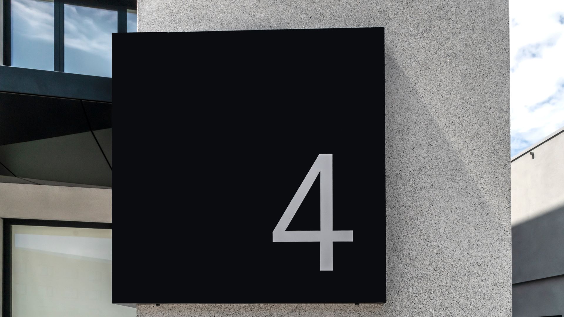 Un grand panneau carré noir orné d'un chiffre 4 argenté, fixé sur un mur de pierre grise.