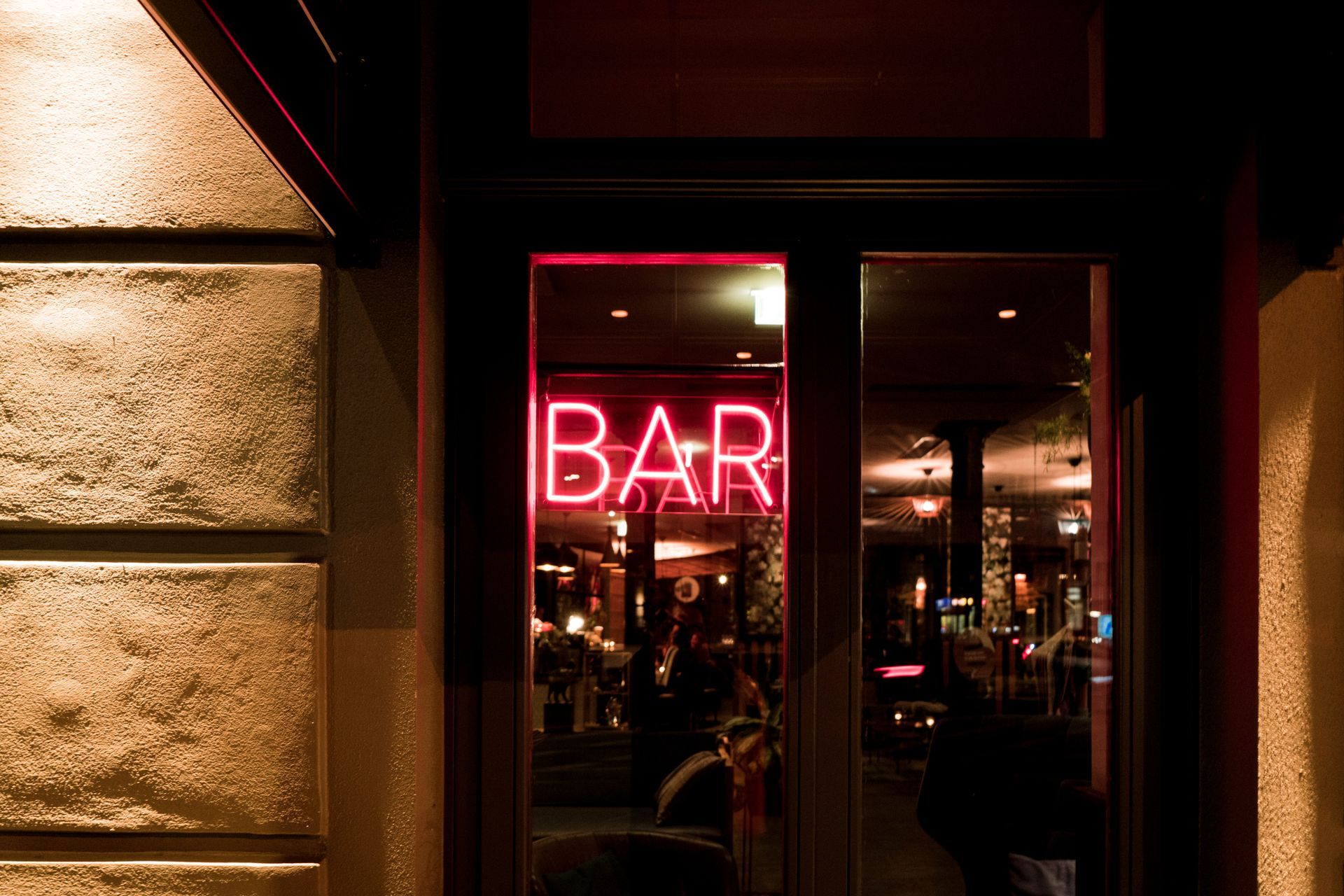 Une enseigne lumineuse rouge BAR au néon est visible la nuit à travers une porte vitrée teintée.