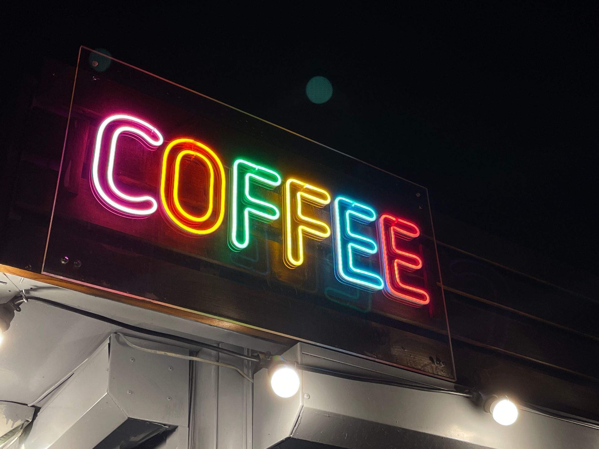 Une enseigne lumineuse nocturne affichant le mot COFFEE en lettres aux couleurs de l'arc-en-ciel sur fond sombre.