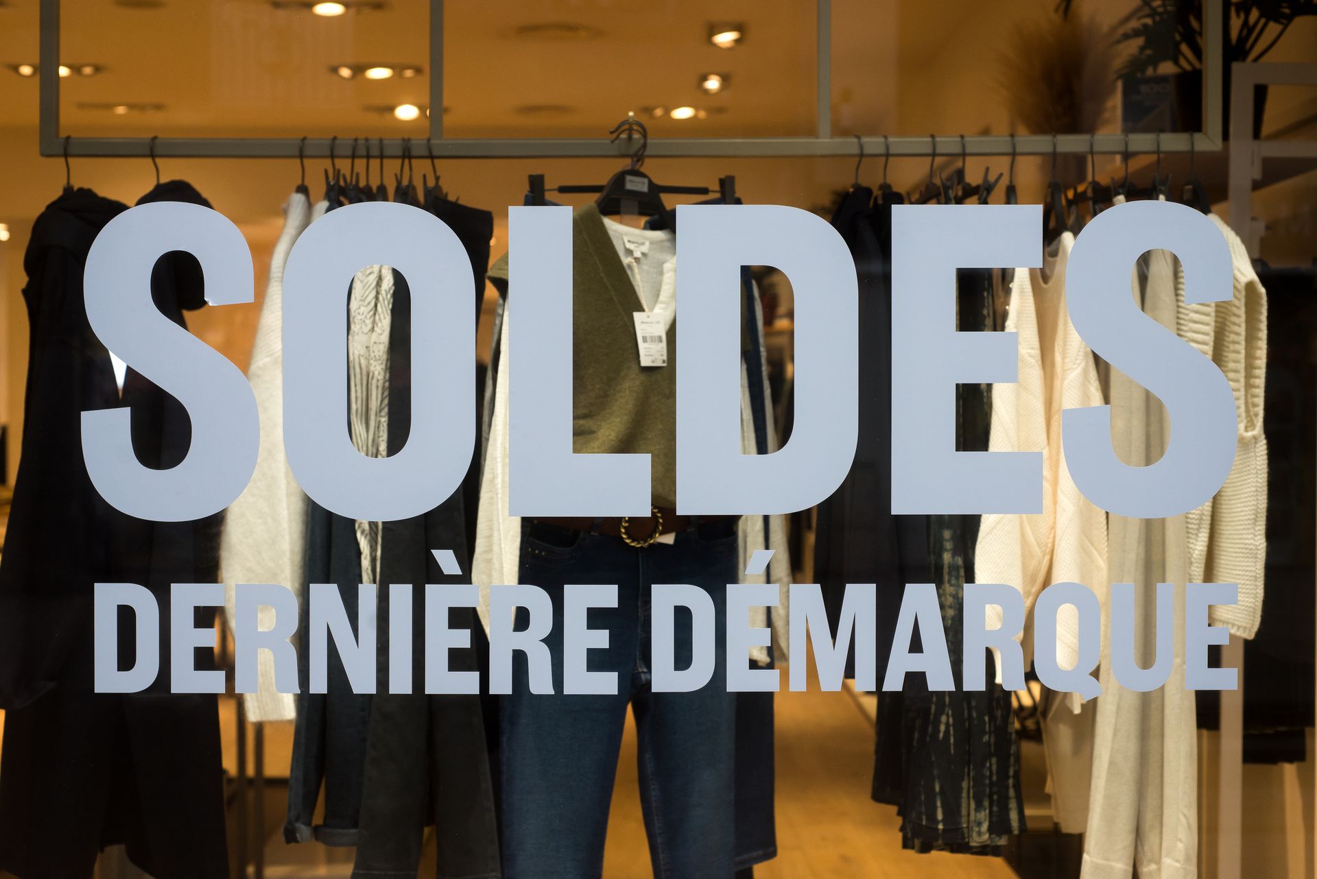 Vitrine d'un magasin présentant des vêtements sur des portants avec un grand texte indiquant SOLDES DERNIÈRE DÉMARQUE.