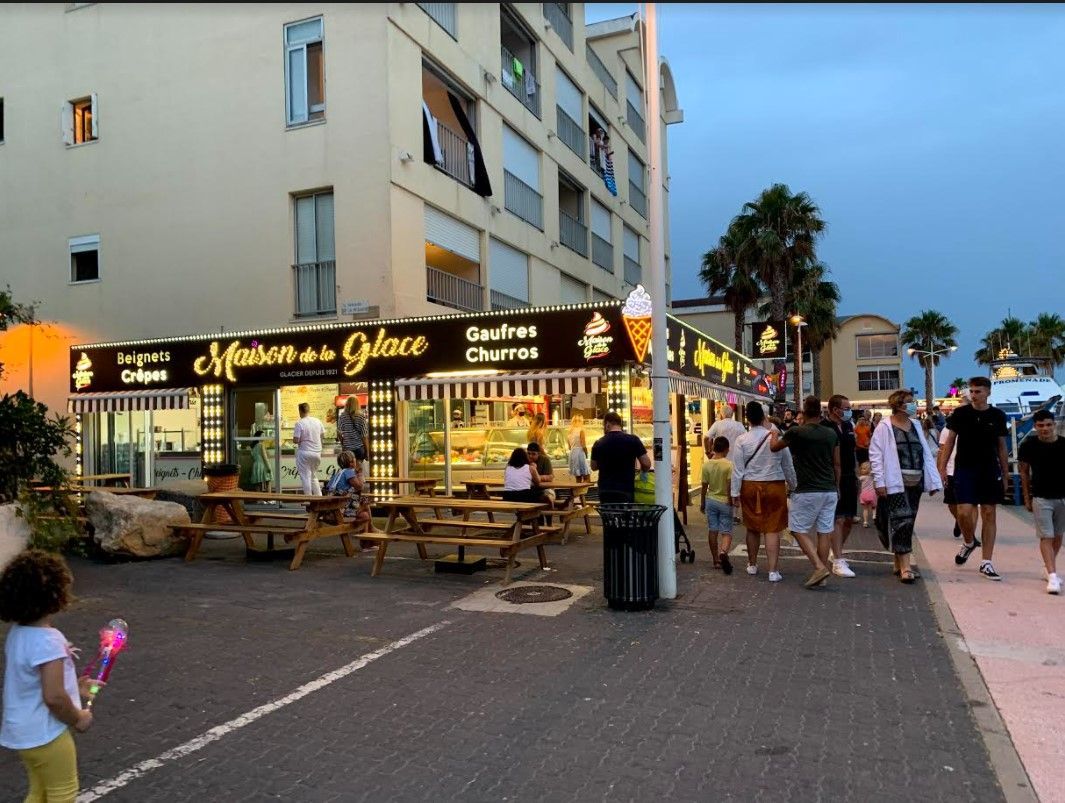 Glacier et crêperie en plein air Maison de la Glace sur une rue animée où les gens se promènent et déjeunent aux tables en terrasse.