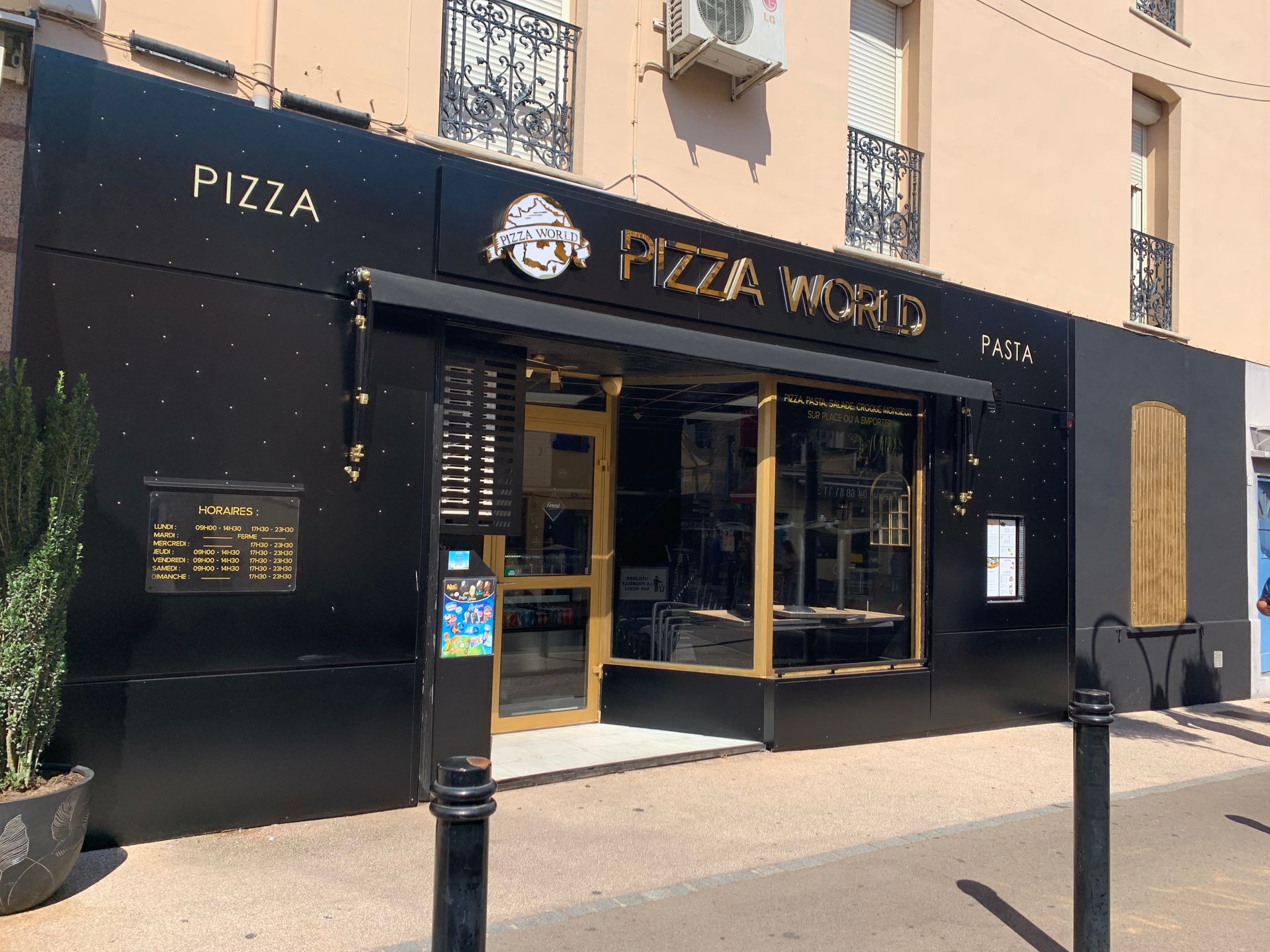 Vue depuis la rue d'un restaurant Pizza World avec une façade noire, une enseigne dorée et une entrée vitrée.