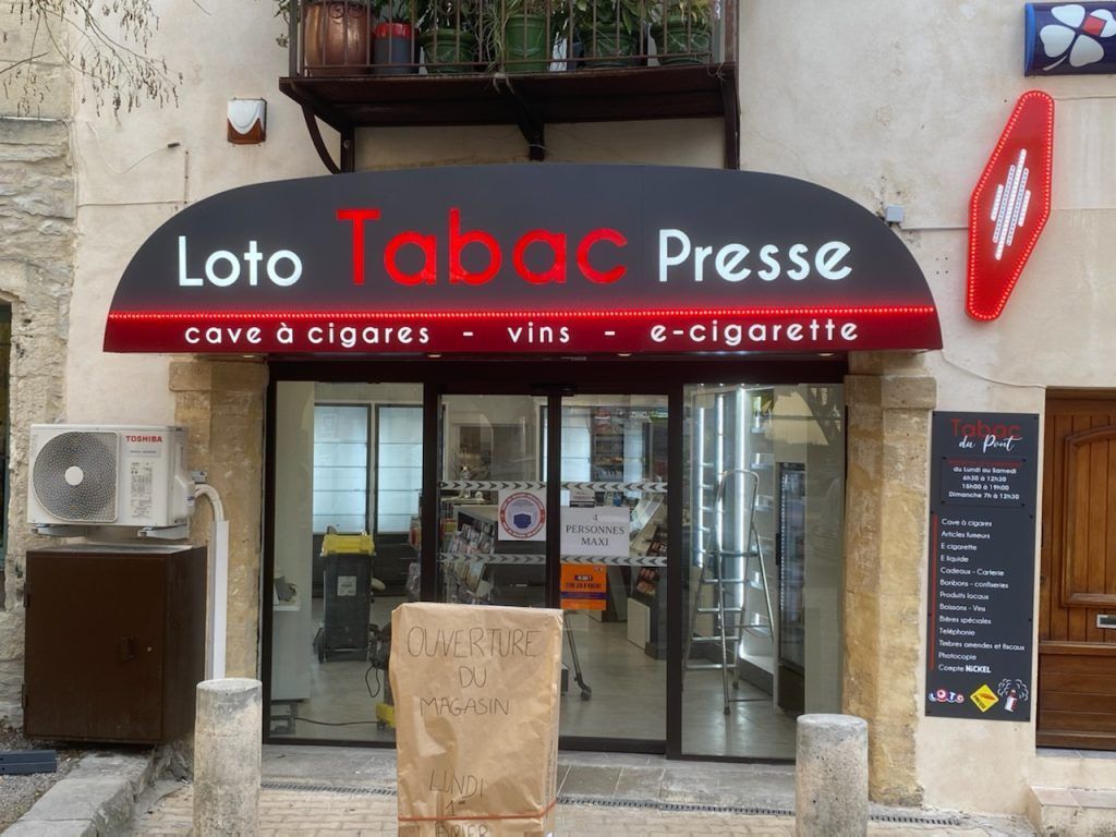 Une devanture de magasin en France, intitulée Loto Tabac Presse, avec des enseignes pour les cigares, le vin et les cigarettes électroniques sur un auvent noir incurvé.