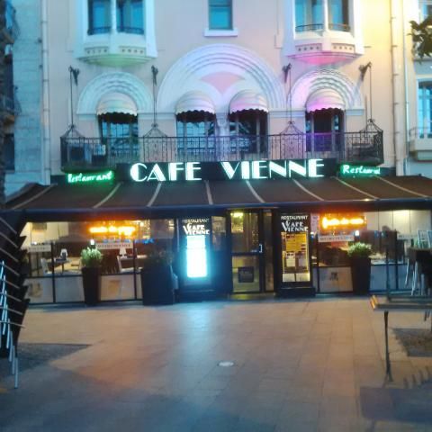 Le restaurant Café Vienne au crépuscule, avec son enseigne lumineuse, son auvent sombre et sa terrasse extérieure.