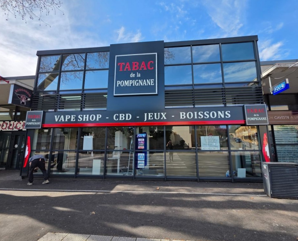 La devanture du Tabac de la Pompignane, avec des enseignes pour le tabac, le vapotage, le CBD, les jeux et les boissons, et une personne à l'intérieur.