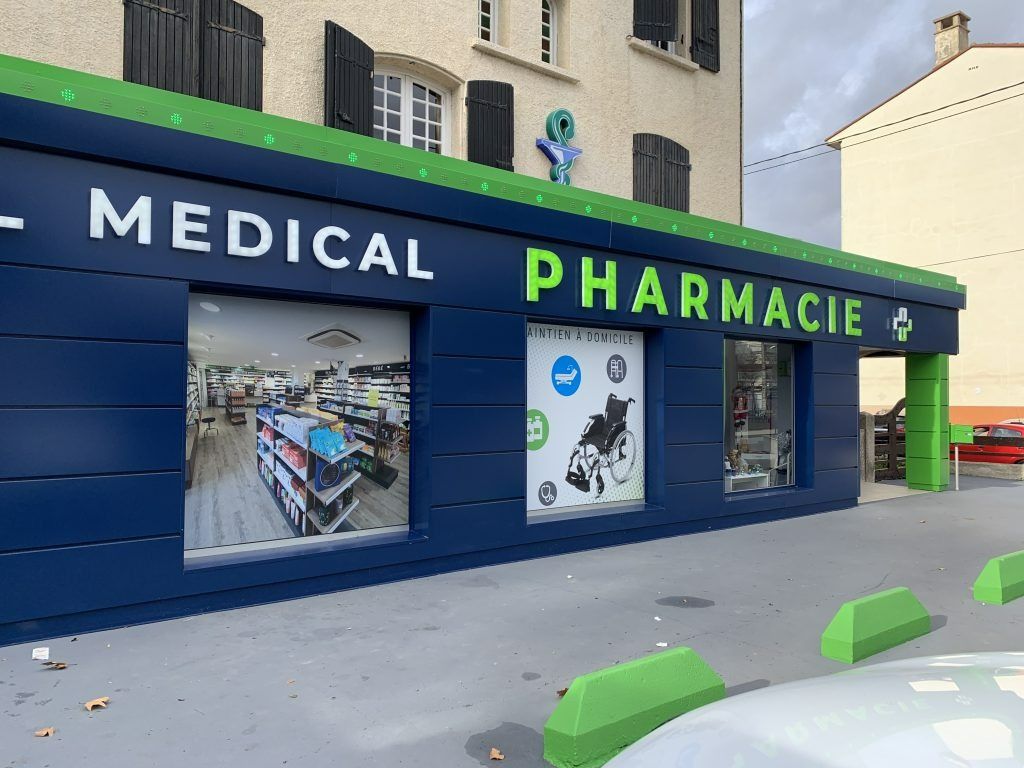 Extérieur d'un bâtiment de pharmacie moderne présentant une façade bleu foncé avec des accents verts et des enseignes indiquant PHARMACIE MÉDICALE.