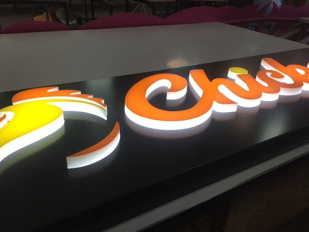 Une enseigne lumineuse en 3D représentant une icône de poulet jaune à côté du texte orange en écriture cursive poussin sur fond noir.