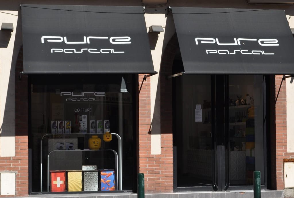 Une devanture de magasin avec deux auvents noirs portant l'inscription pure pascal au-dessus de vitrines et une façade en briques.