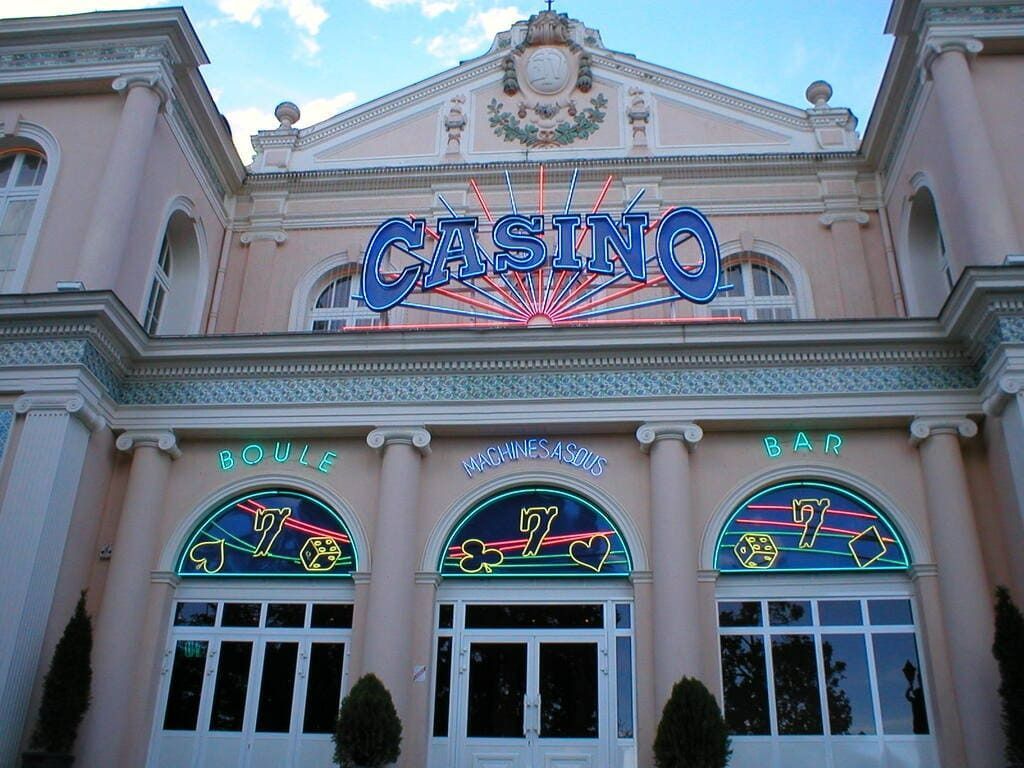 Un bâtiment de casino rose pâle avec des entrées cintrées, des vitraux décoratifs et une grande enseigne lumineuse CASINO.