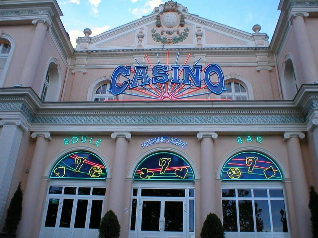 Un bâtiment de casino rose pastel avec des néons au-dessus de trois entrées cintrées ornées de motifs de cartes à jouer.