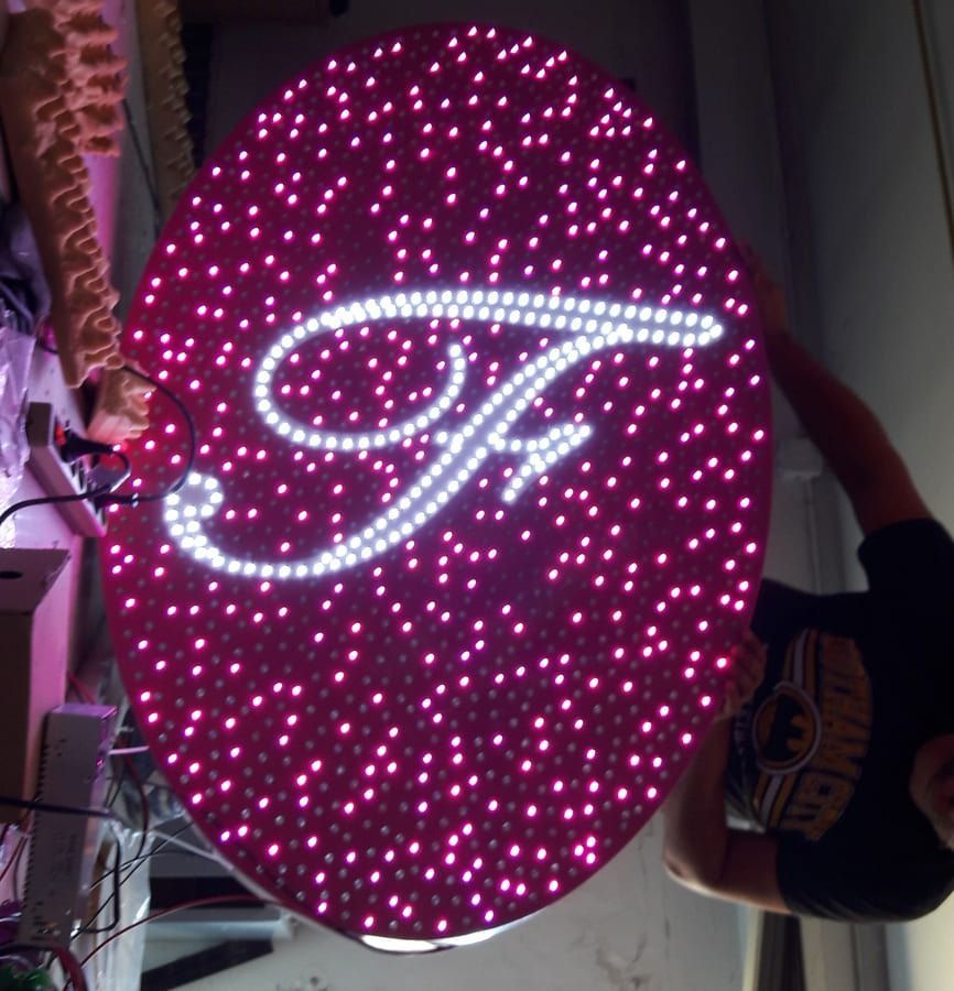 Enseigne LED circulaire personnalisée avec la lettre F en écriture cursive blanche brillante sur un fond dense de petites lumières roses.