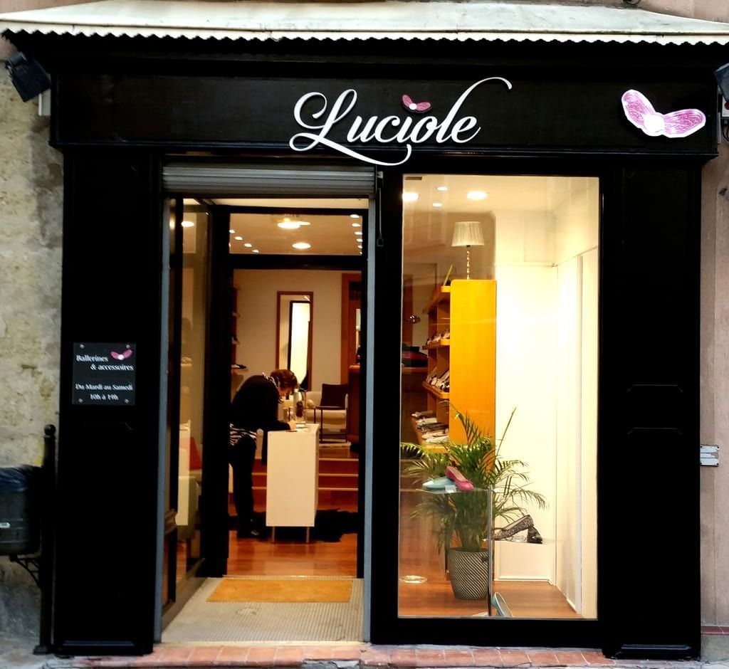 La façade d'un magasin nommé Luciole, avec une façade noire, des portes vitrées et un intérieur jaune vif.