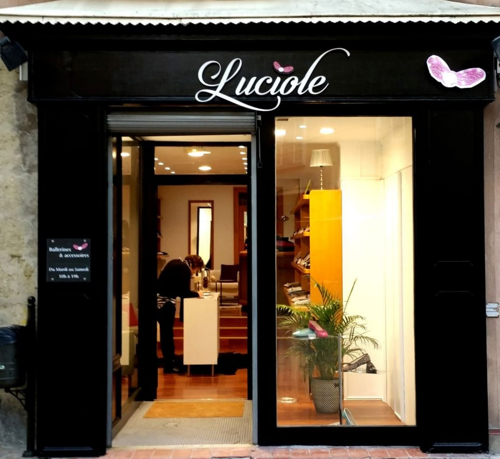 Façade de Luciole, une boutique aux finitions noires, avec une entrée vitrée et un intérieur lumineux agrémenté d'une plante en pot.