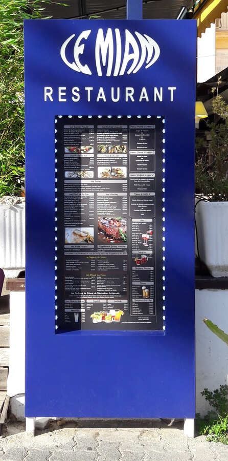Un panneau de menu bleu sur pied pour le restaurant Le Miam, avec un logo blanc en haut et une liste encadrée des plats proposés.