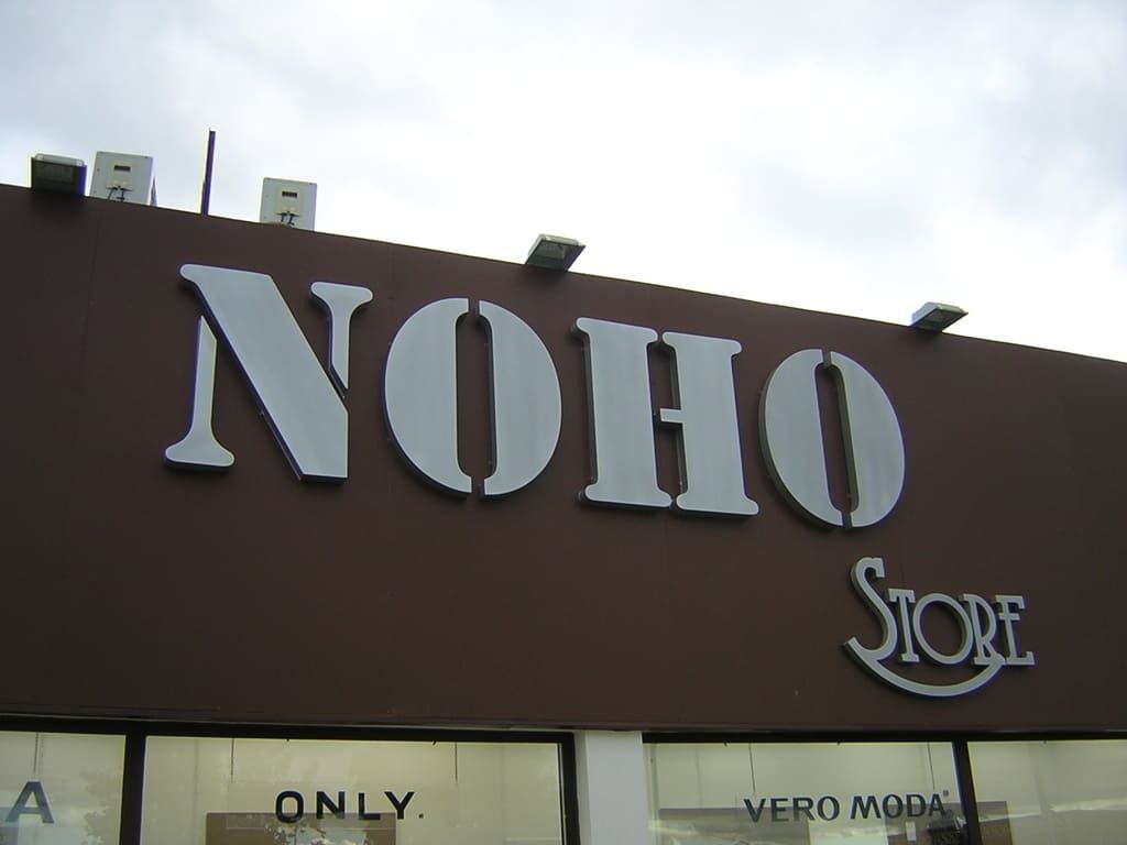 Une enseigne marron devant un magasin indique NOHO STORE en grandes lettres grises, avec les inscriptions ONLY et VERO MODA visibles sur la vitre en dessous.