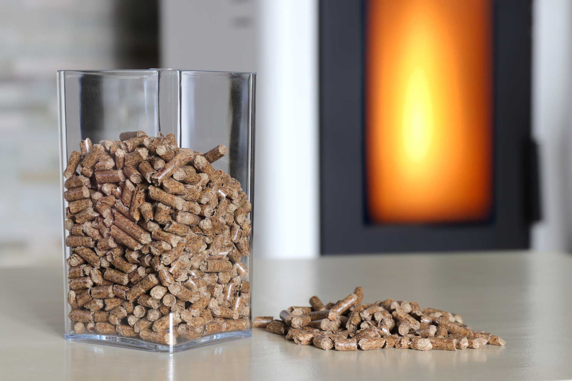 Des granulés de bois dans un récipient en verre devant un âtre