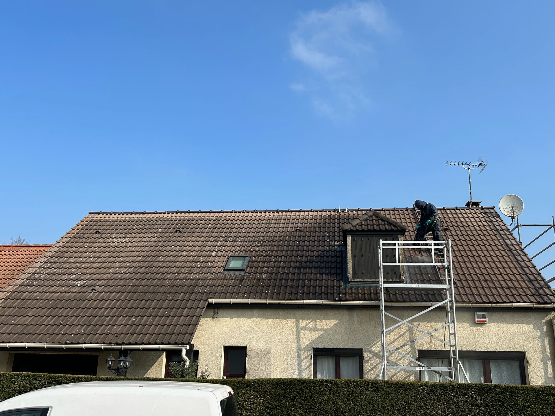 Personne debout sur un échafaudage en train de réaliser le nettoyage d'une toiture au nettoyeur haute pression