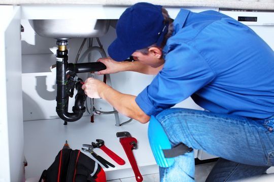 Un fontanero está arreglando un fregadero en una cocina.