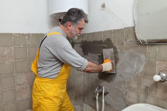 Un hombre con un mono amarillo está enyesando una pared en un baño.