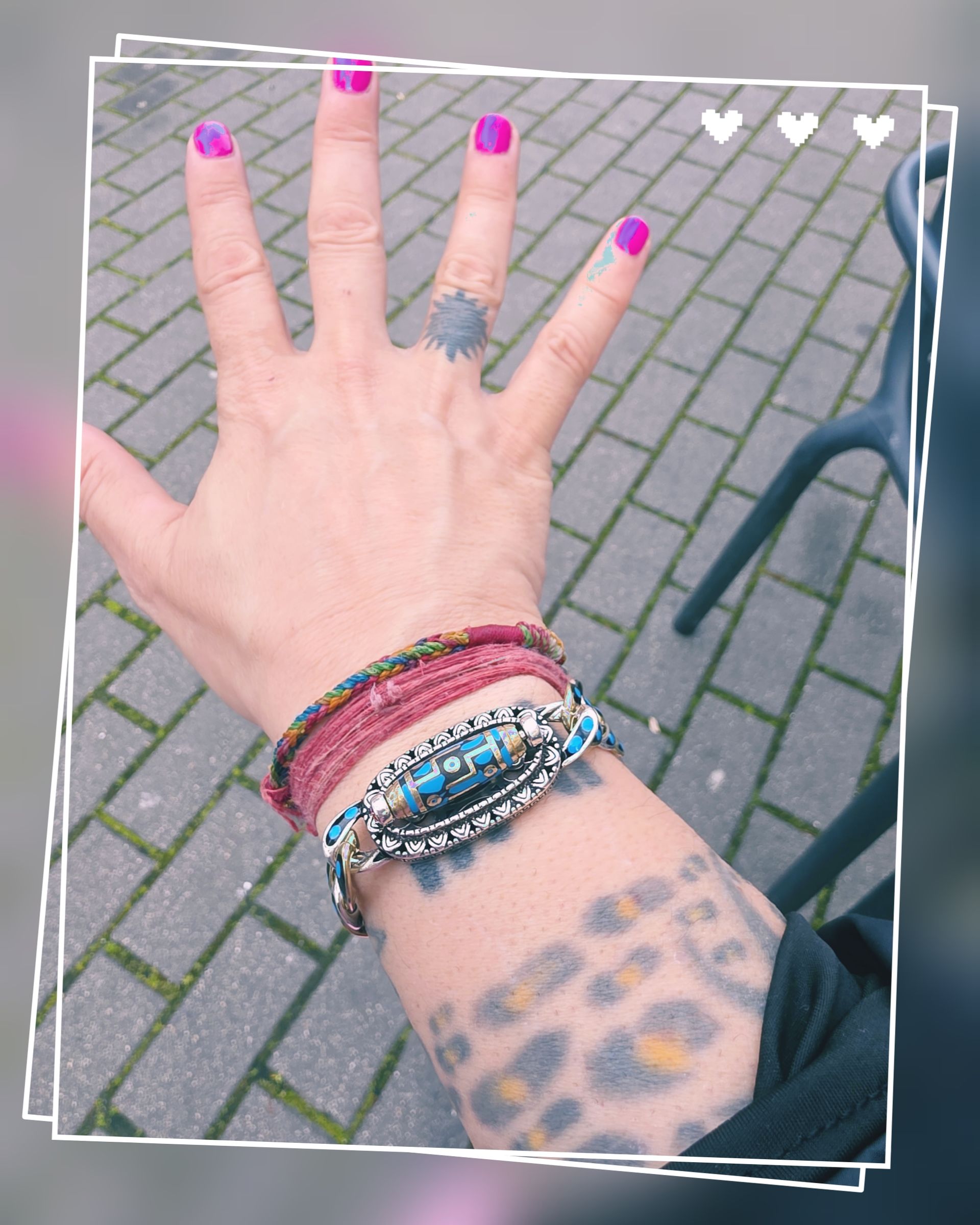 Una mano con esmalte de uñas de color rosa brillante, un anillo de sol y pulseras apiladas, mostrando un tatuaje de estampado de leopardo en el antebrazo.