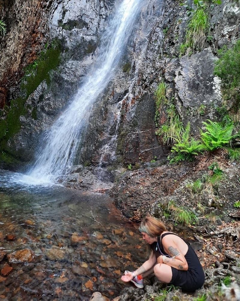 Una mujer está arrodillada frente a una cascada.