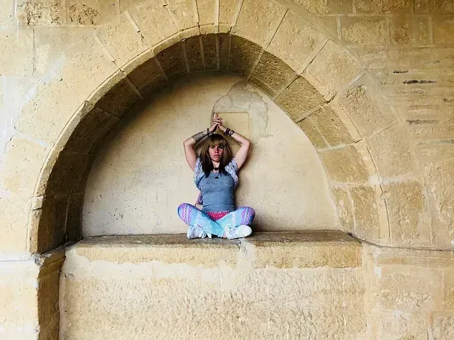 Una mujer está sentada en posición de loto en un arco de piedra.