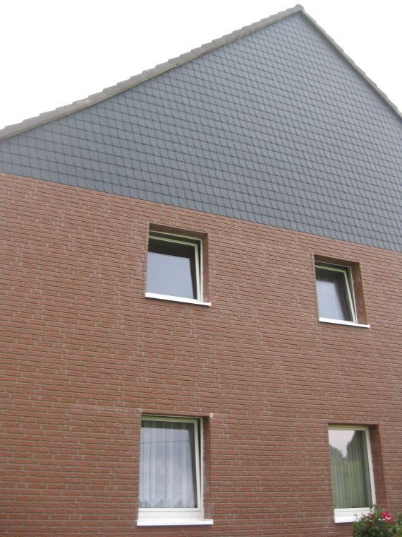 Ein Backsteingebäude mit einem grauen Dach und drei Fenstern