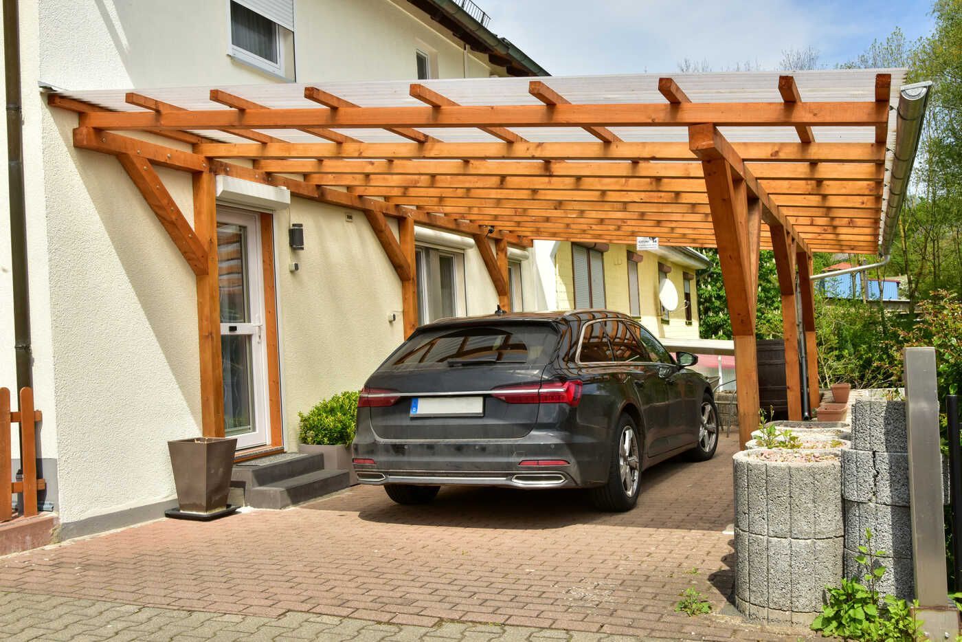 Ein Auto ist unter einem Holzdach vor einem Haus geparkt.
