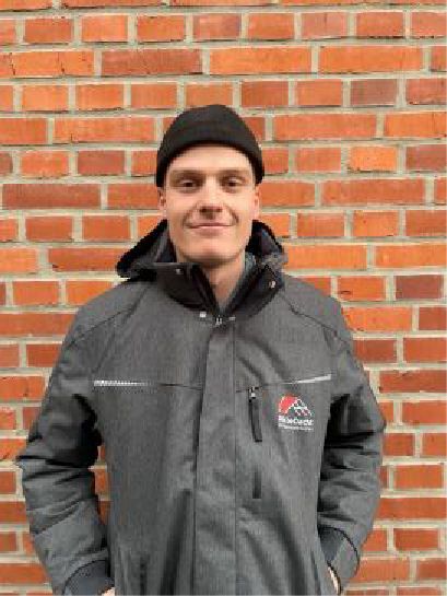 Ein Mann mit Hut und Jacke steht vor einer Backsteinmauer.