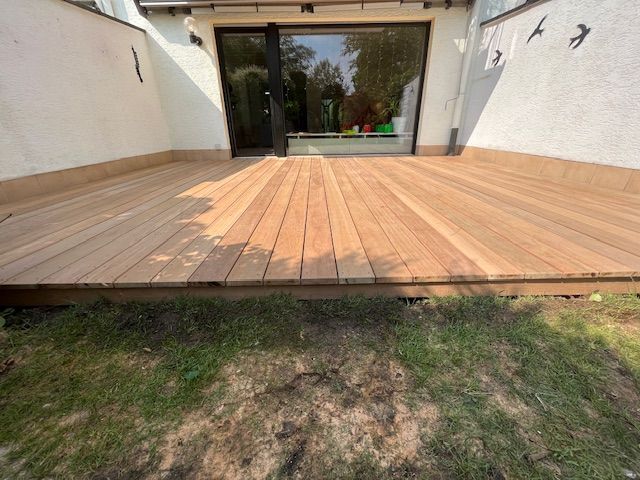 Vor einem Haus liegt im Gras ein Holzdeck. Foto von Dennis Schoo Gartenideen & Gestaltung