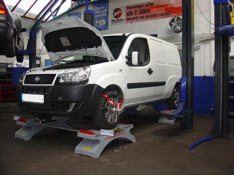 Ein weißer Lieferwagen mit geöffneter Motorhaube steht auf einer Hebebühne in einer Garage