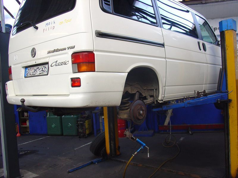 Ein weißer Volkswagen Transporter steht auf einer Hebebühne in einer Garage