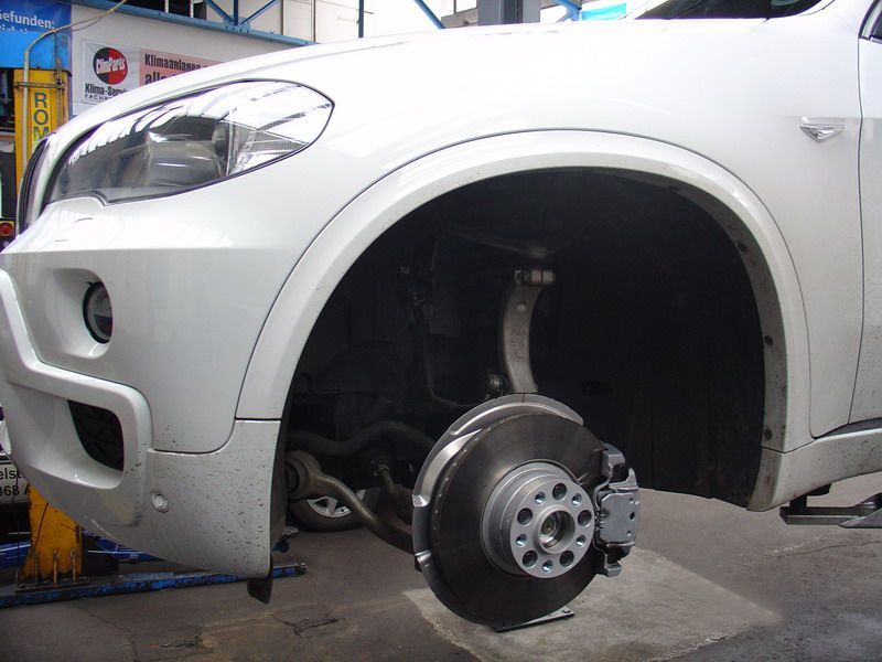 Ein weißes Auto mit einem kaputten Rad steht auf einer Hebebühne