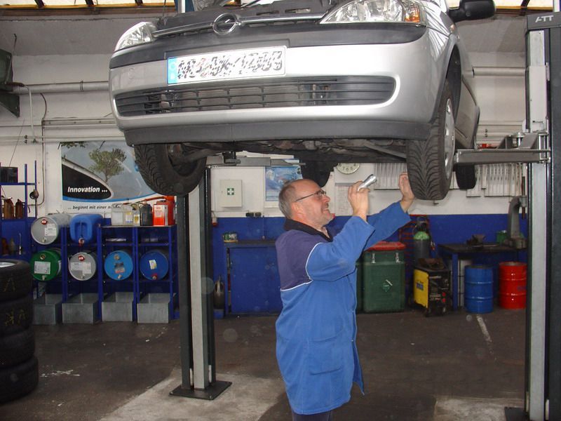 Ein Mann in einer blauen Jacke arbeitet an einem Auto mit einem Nummernschild mit der Aufschrift nk24w1063
