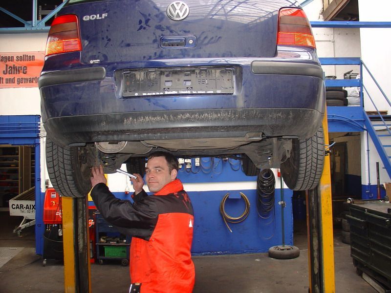 Ein Mann in einer roten Jacke arbeitet an einem Volkswagen Golf