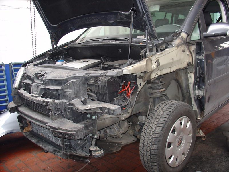 Ein beschädigtes Auto mit geöffneter Motorhaube steht auf einem Ziegelboden