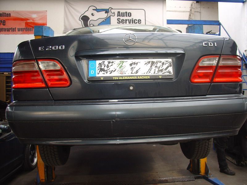 Ein schwarzer Mercedes sitzt auf einer Hebebühne vor einem Schild mit der Aufschrift „Autoservice“