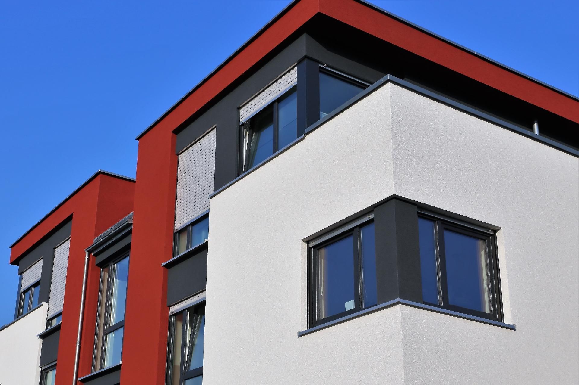 Modernes Wohnhaus mit rot-weißer Fassade und blau umrandeten Fenstern vor klarem Himmel