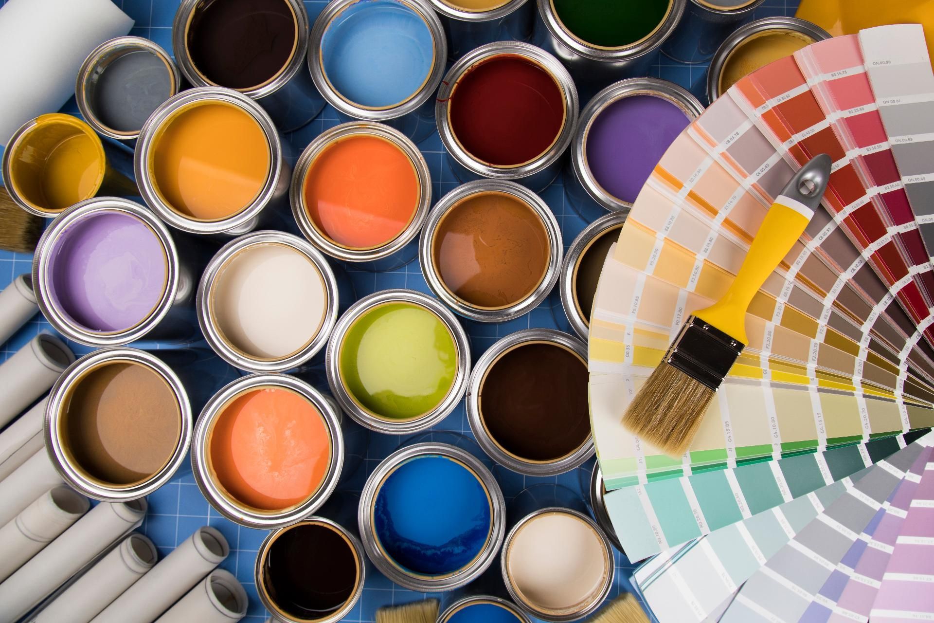 Bunte Farbdosen und ein Fächer mit Farbmustern, die zu einer farbenfrohen Palette angeordnet sind.