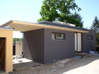 Modernes graues Gebäude mit Carport, weißer Tür und kleinen Fenstern