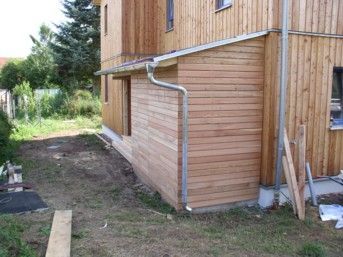 Holzhausfassade mit hellbrauner Verkleidung und einem kleinen angebauten Schuppen.