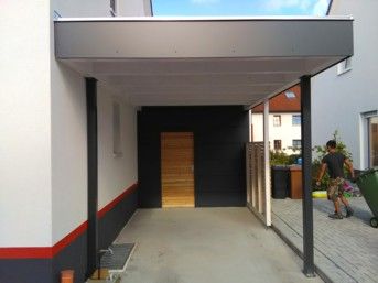 Carport mit dunklem Rahmen und Dach, weißen Wänden