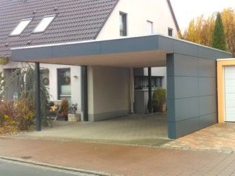 Grauer Carport an einem weißen Haus, auf einer gepflasterten Auffahrt.